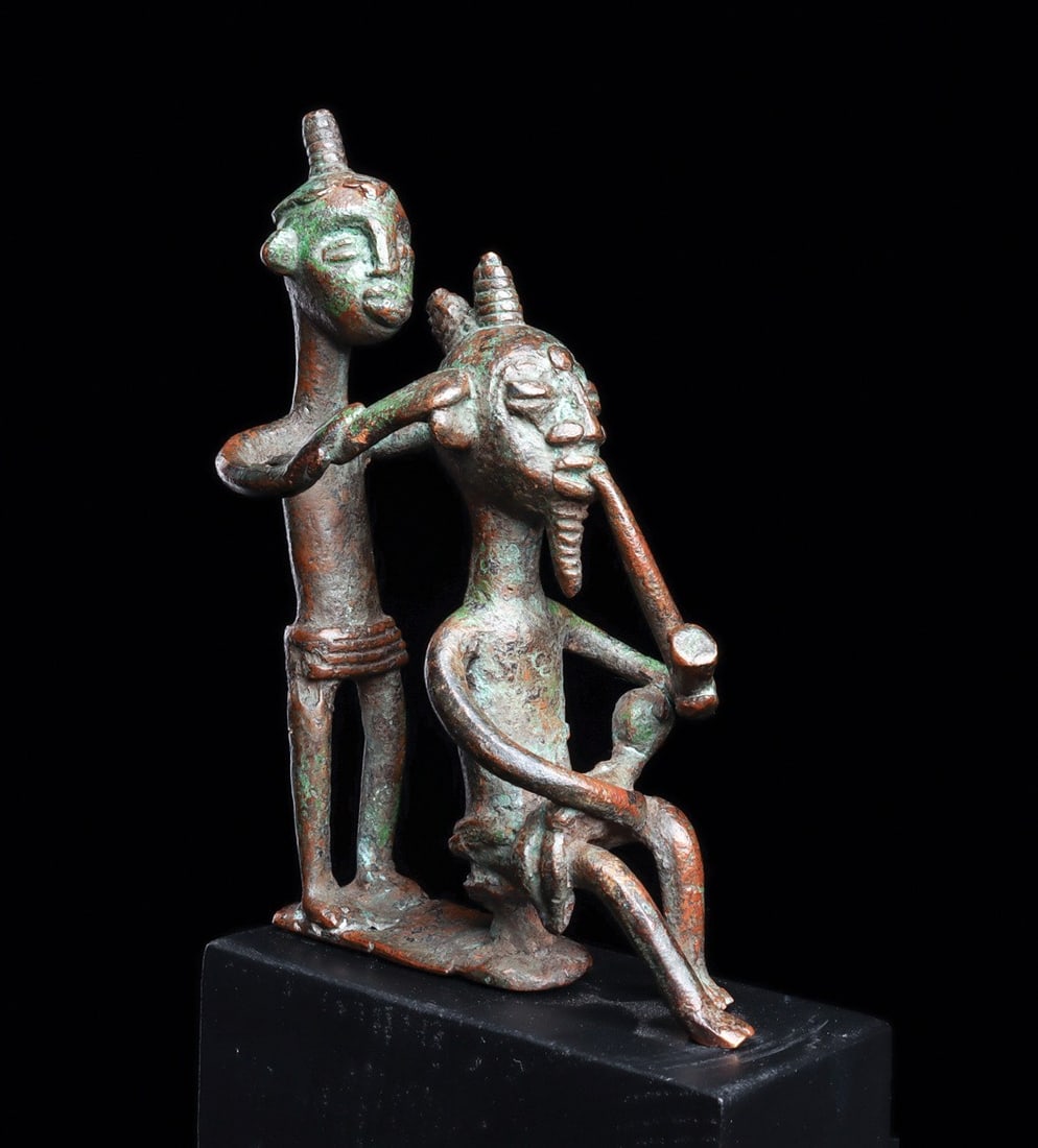 Ashanti Bronze: Ghana. Copper alloy of a seated male figure smoking a pipe, and cradling a small child in his lap. An attendant is standing behind with both hands at sides of the head possibly grooming his hairdo. Gr