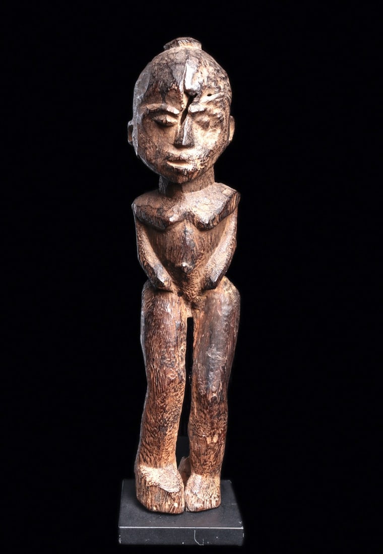 Lobi Figure: Burkina Faso. Very old carved wood figure, standing with long separated legs, her short torso with relief arms bent at sides, the rounded face with heart shaped face, and relief disc atop head. Eroded