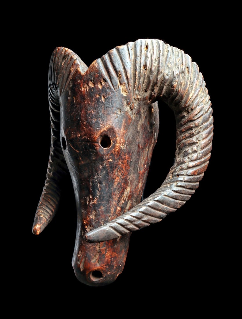 Bozo Ram Head: Mali. Carved ram head having thick, coiling horns with deep grooved texture, long tapered face with hollowed eyeholes and nostrils. Deep brown patina. Weathered, minor loss. Modern hanging hook on