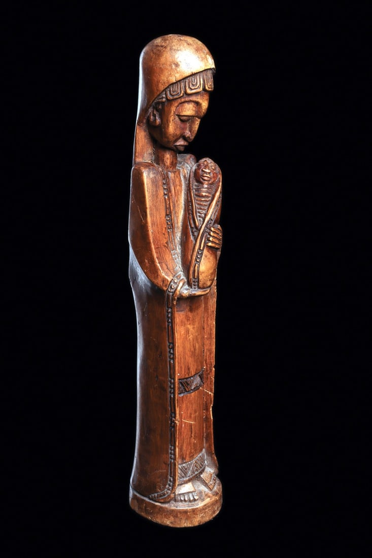 Madonna and Child Figure: Angola or DRC. Elongated and slender wood carving of the Virgin Mary with downcast gaze, tenderly holding the swaddled baby Jesus. Concave integral base. Minor surface wear at edges. Medium brown