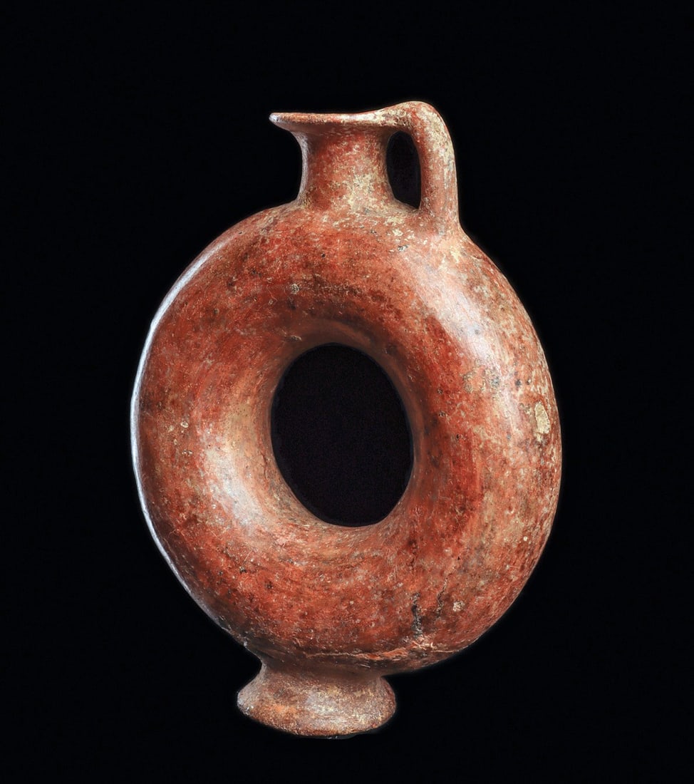 Impasto Ware Ring-Body Oinochoe: Eastern Mediterranean. Ca. 6th century BCE. Salmon color pottery oinochoe, having a ring shape body standing on an integral low pedestal foot, short neck with a flared rim having a handle from the lip