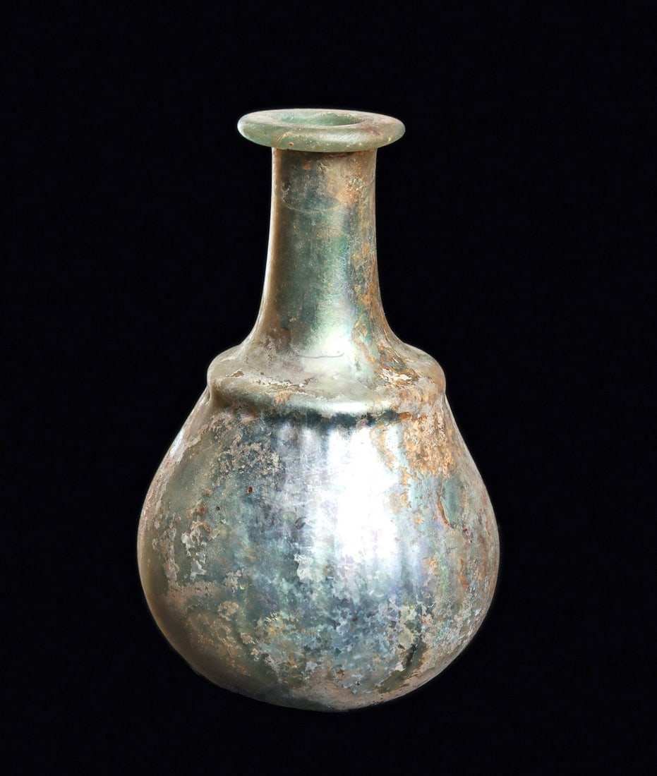 Roman Ribbed Glass Bottle: Eastern Mediterranean.Ca. 3rd to 5th century CE. Blue-green blown glass bottle, having a vertical ribbed dip molded tapered bulbous body, capped shoulder and tapered cylindrical neck with a flat rolle