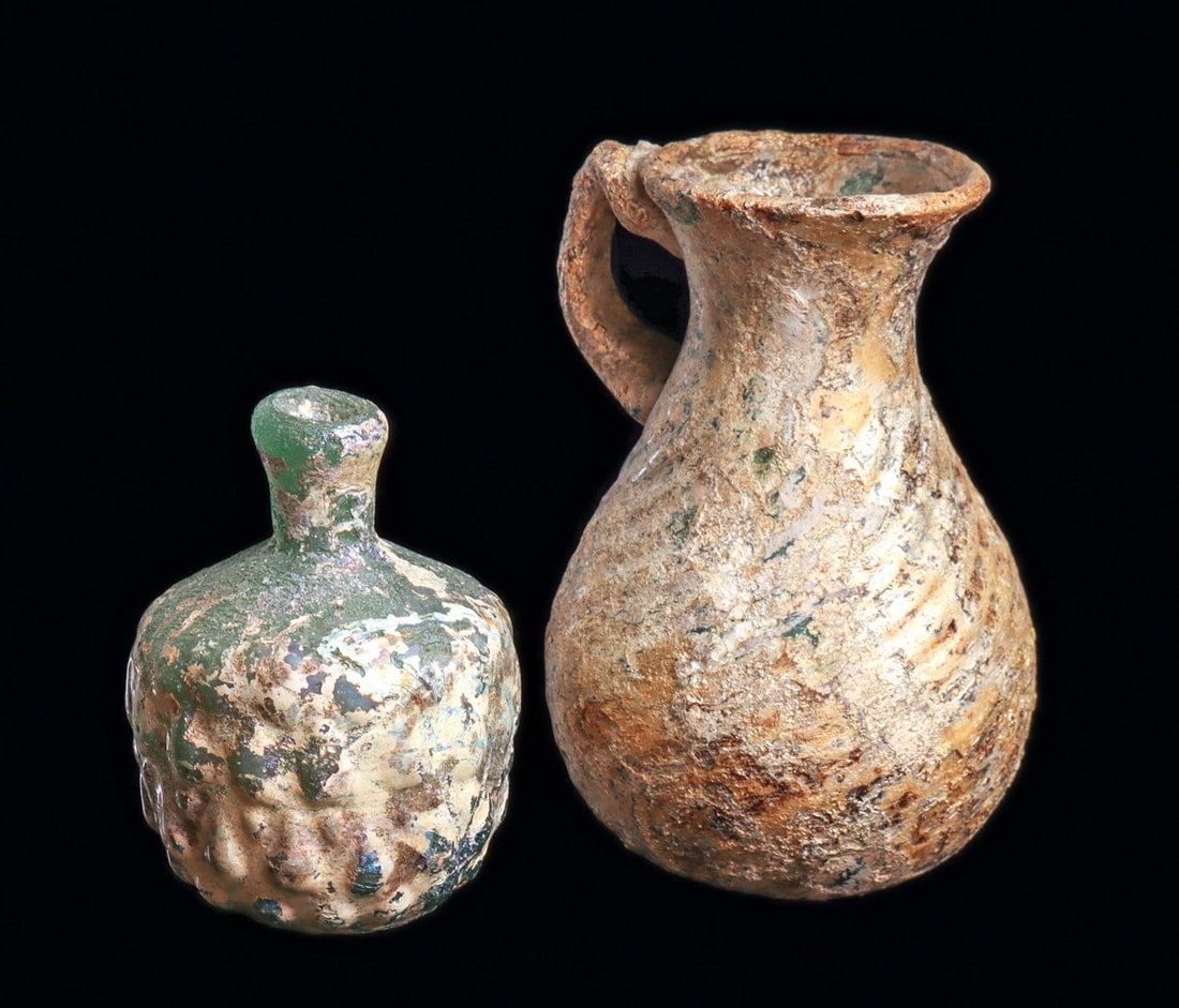 Late Roman/Byzantine Blue-Green Vessels (2): Eastern Mediterranean. Ca. 4th - 8th century CE. Two different blown glass examples including a blue-green dip molded large pear shape jug having a thick applied handle and a swirl pattern body decora