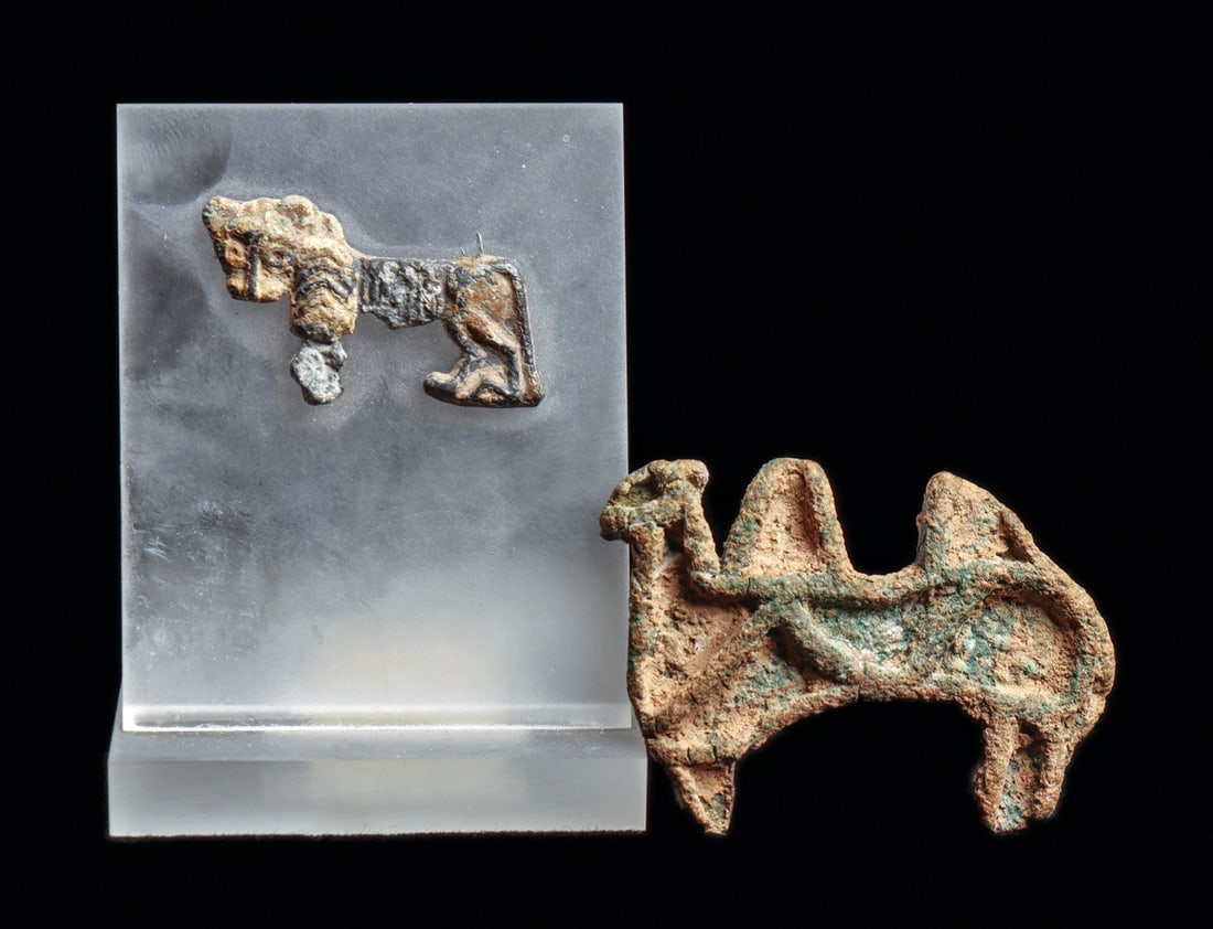 Bactrian Camel Seal & Western Asiatic Lead Lion Applique (2): Central Asia. Ca. 1st millennium BCE. Bronze stamp seal in the form of a camel with two large humps, zig-zag body decoration, suspension loop on the reverse. Over heavy surface encrustation and scatte