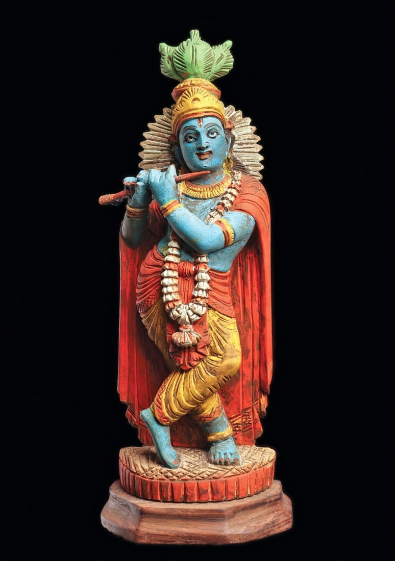 Polychrome Krishna Figure: India. Mid 20th century. Carved polychrome painted wood dancing Krishna figure, wearing a fancy headdress with a triple leaf finial and feathered backsplash, wearing a long floral necklace and long dr