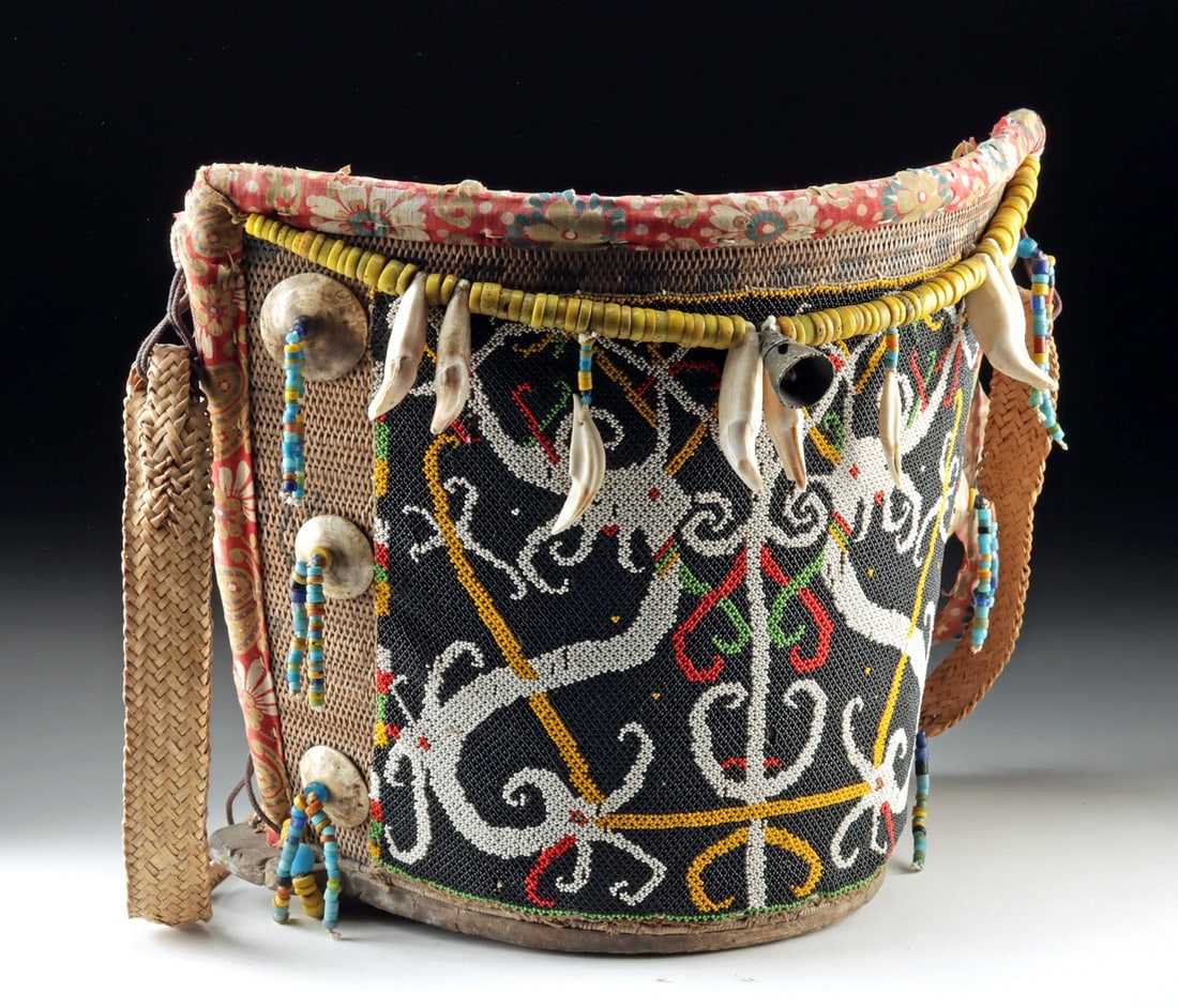 Borneo Dayak Beaded Baby Carrier w/ Bear Teeth & Shells: Southeast Asia, Indonesia, Borneo, Kenyah Dayak, ca. early to mid-20th century CE. A child carrier composed of densely woven rattan attached to a half-circle wooden base, lined with printed cotton clo