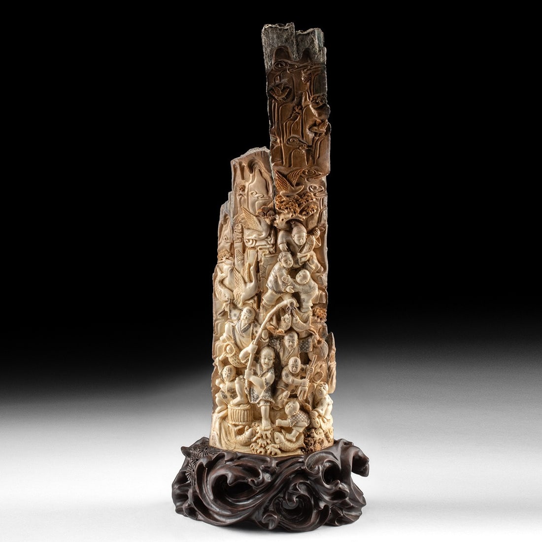 Japanese Mammoth Ivory Relief Fishing Scene: East Asia, Japan, ca. 20th century CE. A mammoth ivory tusk section carved in high and low relief across its entire circumference, the natural taper and cementum rind of the upper portion left largely