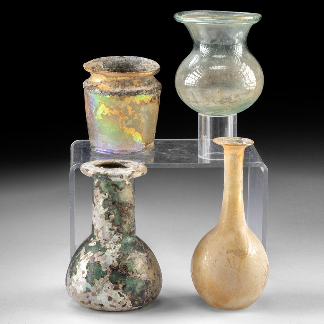 Set of Four Iridescent Roman Glass Vessels: Roman Empire, Levant, most likely Israel or Lebanon, ca. 2nd to 3rd centuries CE. Nice group of early glass vessels. Starting with a stout unguent or balsamarium with heavy bulbous base, thin neck and