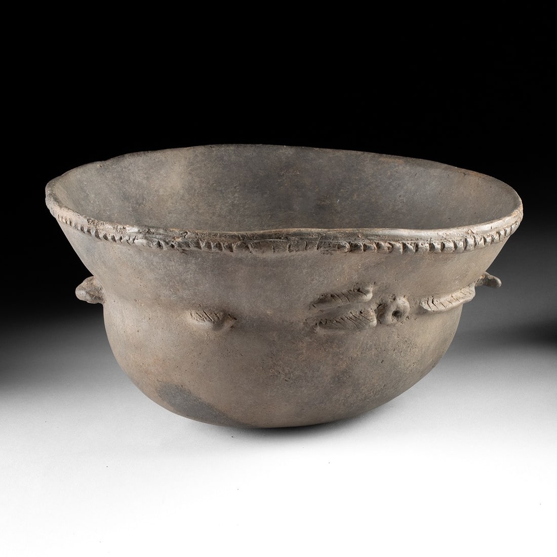Mississippian Fish Effigy Helmet Bowl - Incised: A fish emerges in three-dimensional increments from the walls of this Mississippian effigy bowl, its head thrust forward from the upper shoulder, its paired fins projecting laterally at mid-body, and 