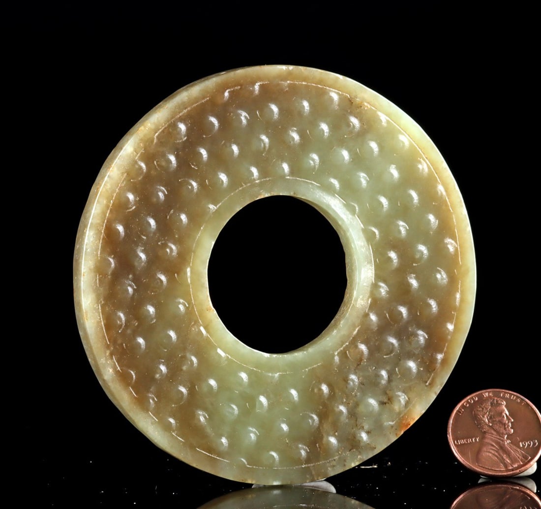 Chinese Nephrite Jade Bi Disc: Far east, China, ca. 2nd half 20th century CE. A carved nephrite jade bi disc of classic circular form, the pale celadon stone displaying soft translucency and natural clouding. One face is decorated 