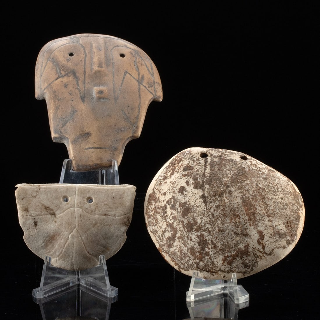 Mississippian Shell & Stone Gorgets - Effigy Face: North America, Mississippian to Fort Ancient, ca. 1000 to 1600 CE. A compelling ensemble of three ancient gorgets, including a finely carved human head effigy in dense fine-grained stone with crisply 