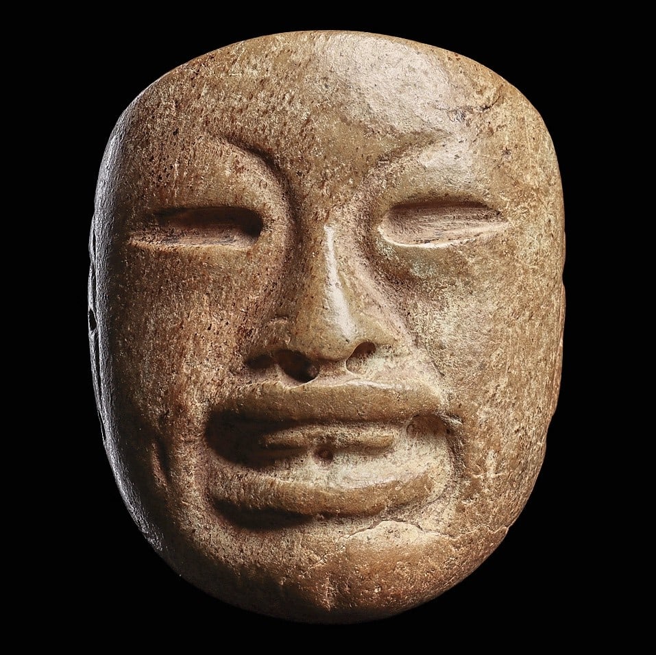 Olmec Serpentine Maskette: Olmec regions, ca. 1000 - 600 BCE. Carved grayish-green serpentine stone maskette having well carved, expressive facial features, broad nose with drilled nostrils, parted lips with upper teeth, drille