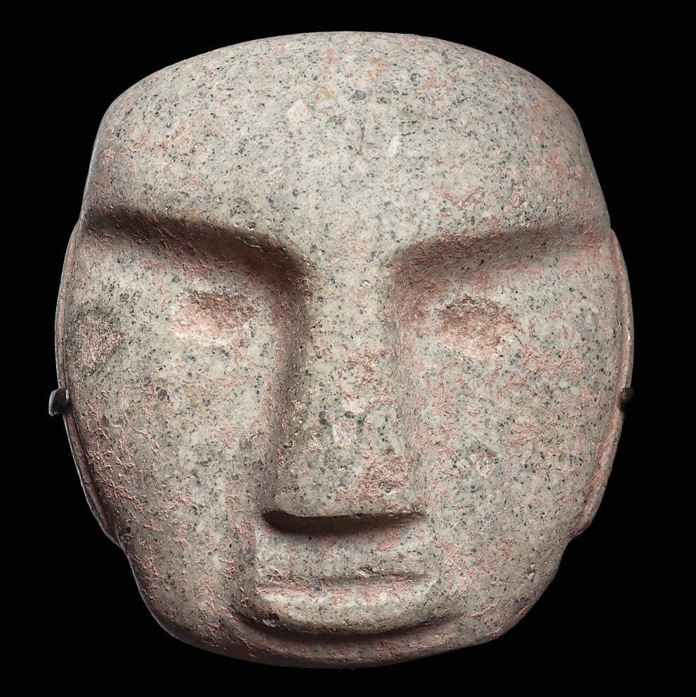 Mezcala Speckled Serpentine Human Face Mask: Guerrero, ca. 400 BCE. Carved speckled greenish-cream serpentine human face mask, depicted with semiabstract facial features having a heavy angular brow line, wide tapered nose and round pecked recess