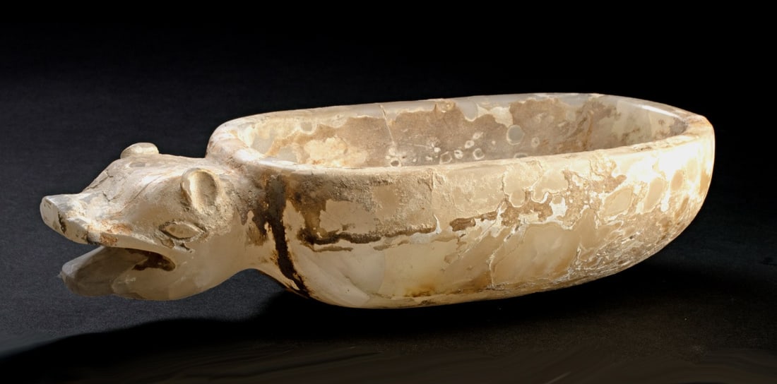 Rare Mixtec Alabaster Bowl - Jaguar Form: Pre-Columbian, Mexico, Mixtec culture., ca. 500 - 800 CE. Carved alabaster oval bowl having a projecting jaguar head at one end, depicted with rounded perked ears, open mouth. Tail curled around the r