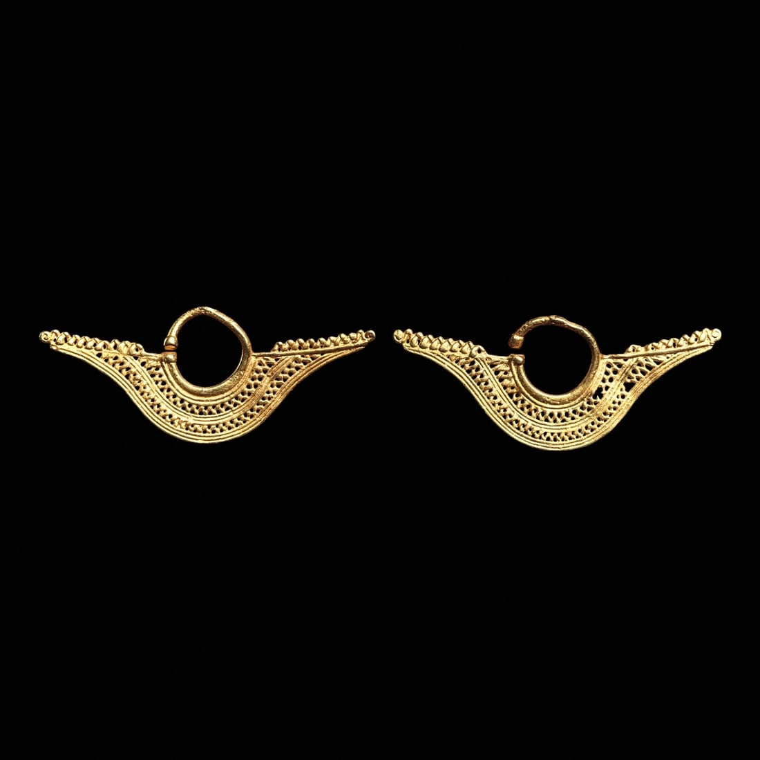 Sinu Gold Filigree Ear Ornaments (2): Sinu, Colombia, ca. 800 - 1450 CE. Matching pair of cast gold ear ornaments, of crescent form with side wings, having two bands of openwork diamond net design. Upper wing bar decorated with zigzag ele