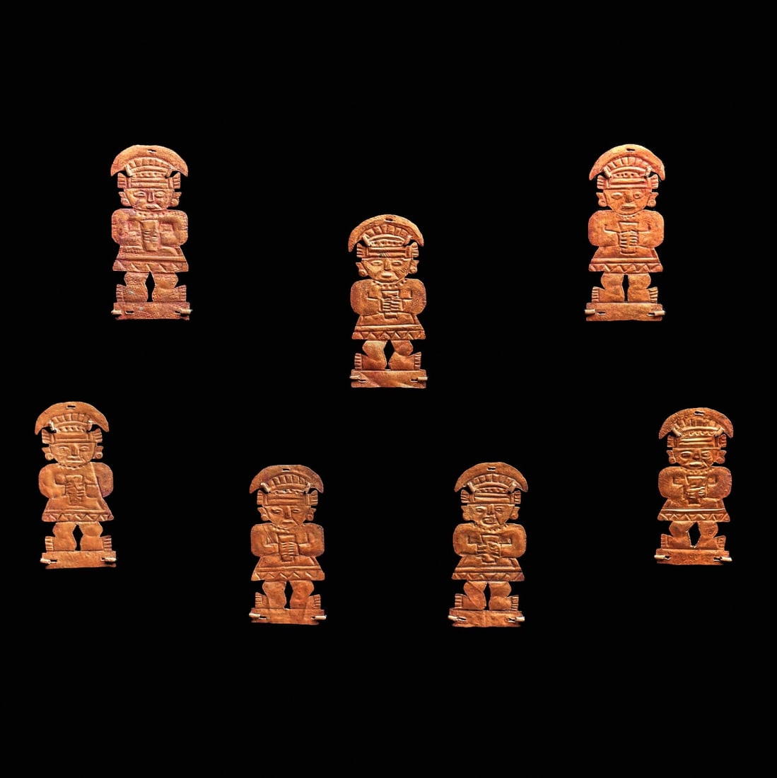 Chimu Copper Figural Appliqués (7): North coast., ca. 1000 CE. Seven matching, beautifully detailed, sheet copper appliqués, each depicting a standing lord or king wearing a crescent shape headdress and short tunic. Each holds a ce