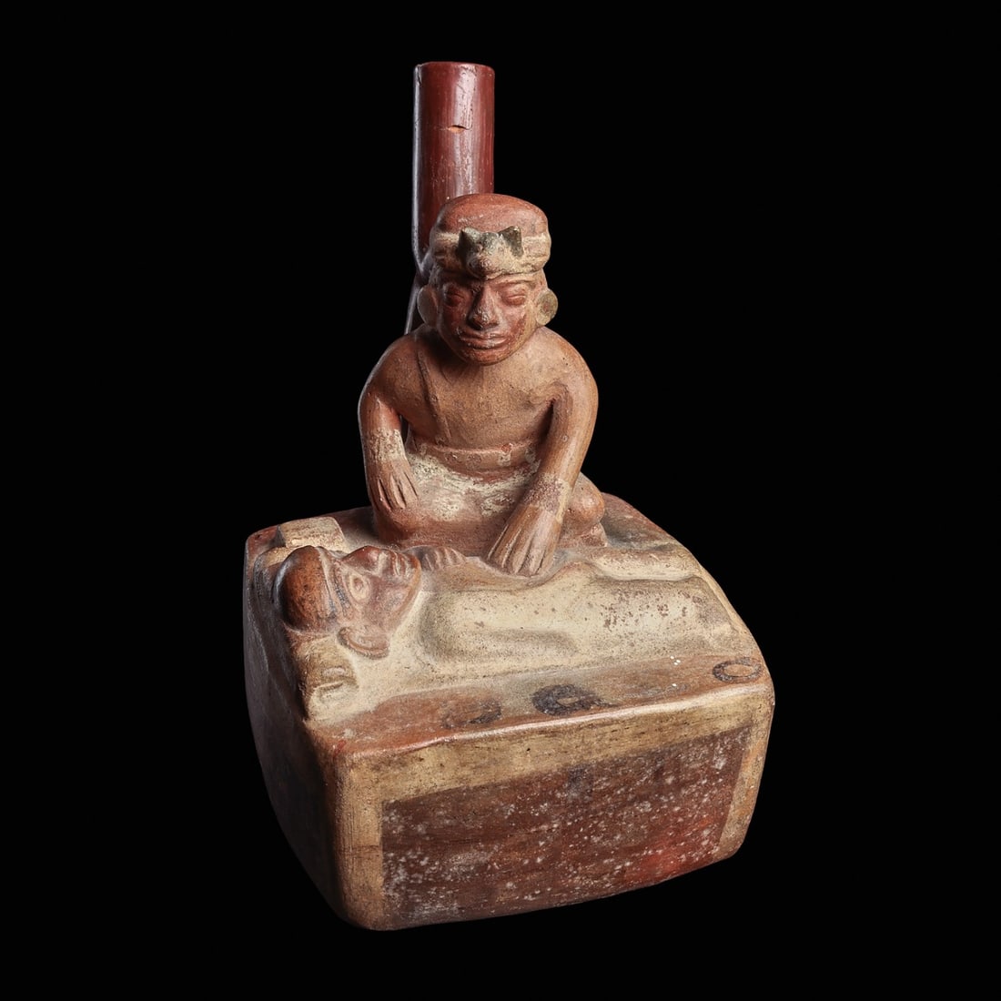 Moche Shamanic Stirrup Spout Vessel: Moche, ca. 500 - 800 CE. Pottery vessel having a stirrup type spout, depicting a scene of a shaman attending to and sitting next to a patient lying on his back with half of his torso exposed. Shaman i