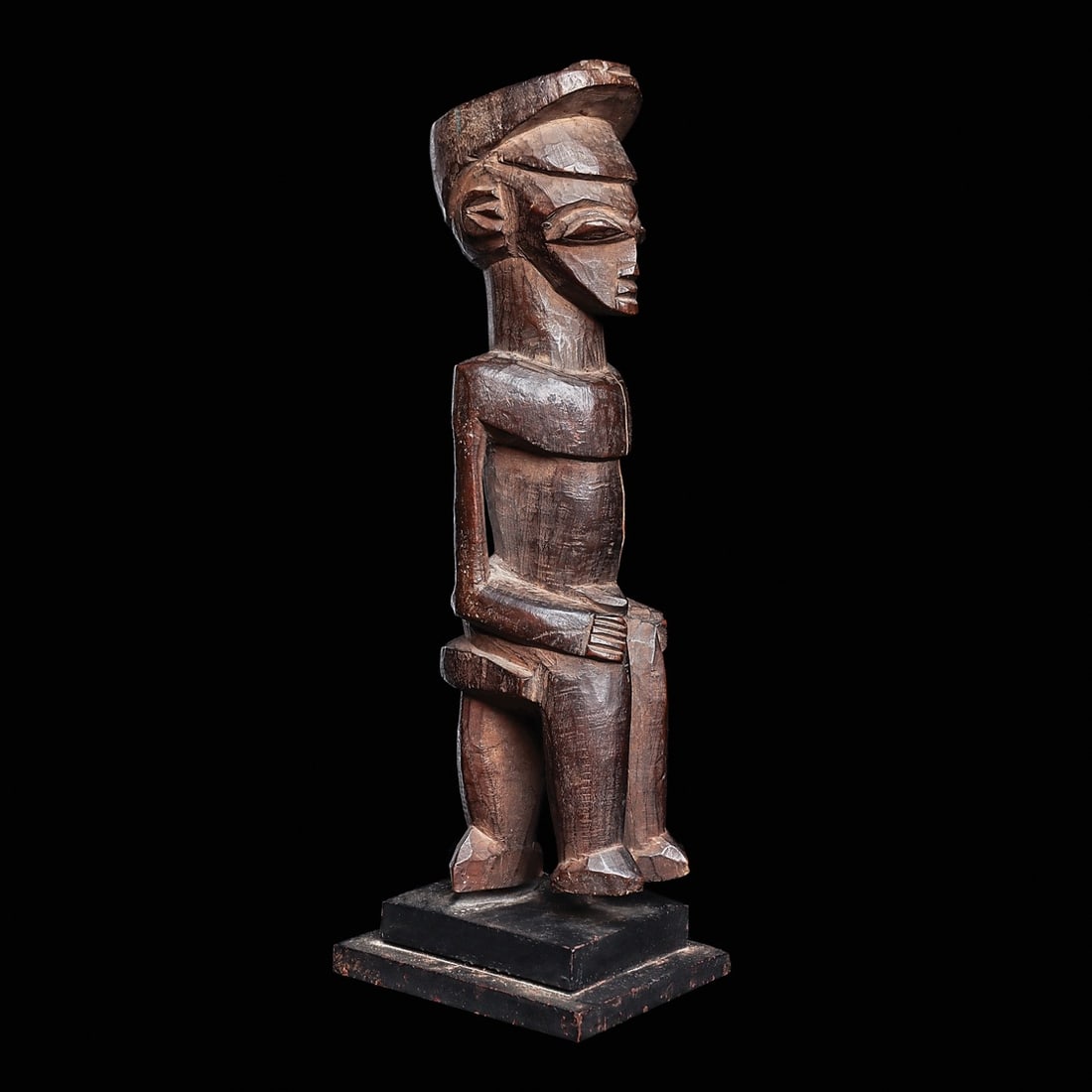 Seated Lobi: Burkina Faso, . Well carved figure of an official wearing a kepi, with relief motif on top. Balanced on seat with legs dangling. Custom base.7”H (17.8cm). Provenance: Collection of Dr. Oliver