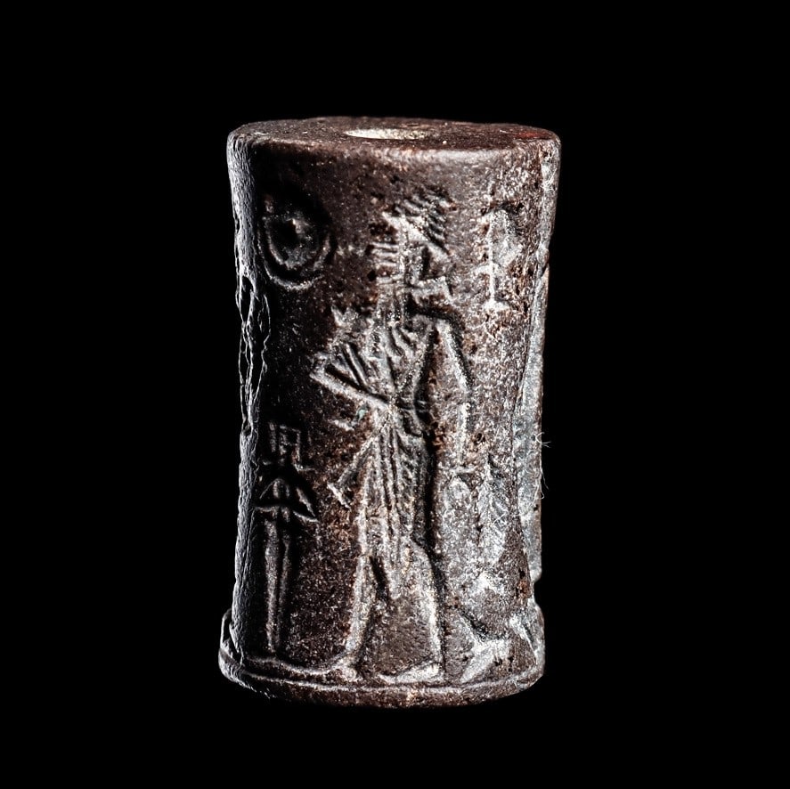 Old Babylonian Hematite Cylinder Seal: Ancient Near East. Mesopotamia, ca. 1900 - 1700 BCE. Carved black hematite cylinder seal having a carved rollout impression depicting a hero kneeling on a platform with upturned lion held above, anoth
