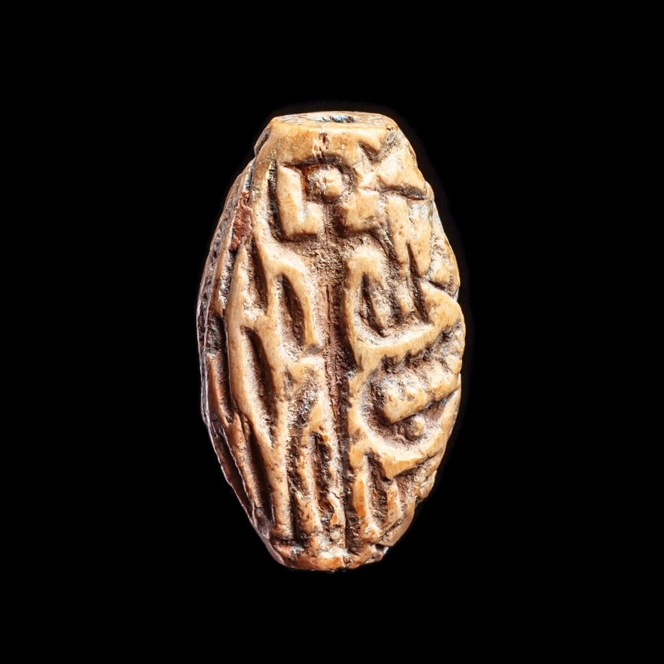 Mesopotamian Carved Stamp Bead: Mesopotamia, ca. 2500 - 1750 BCE. Tooth ivory ovoid bead having a deeply carved stamp impression on both sides. Side A: depicts a stylized tall human figure carrying a basket type object in his right 