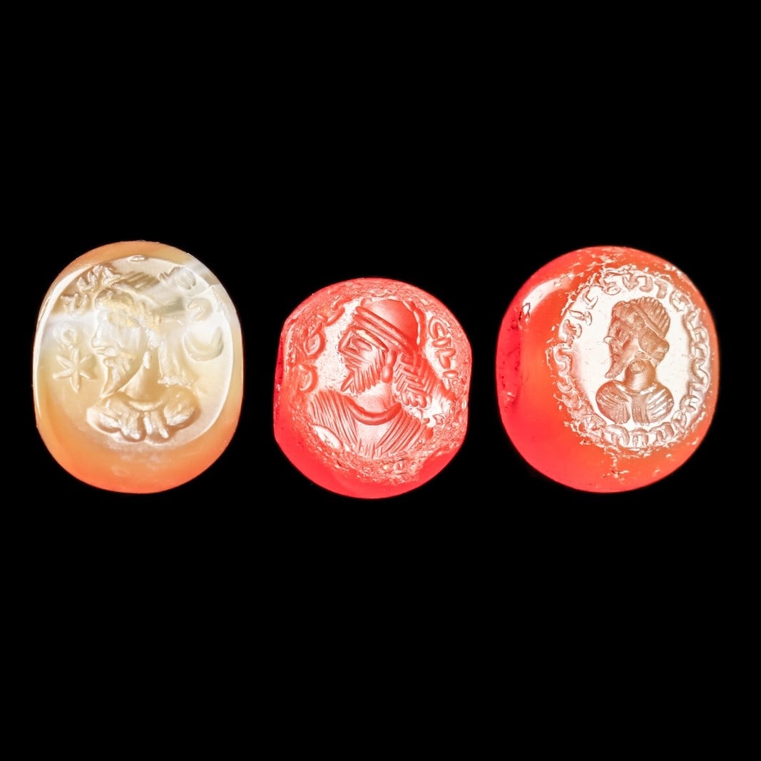 Sasanian Stamp Seals (3): Sasanian Empire, Western Asia, ca. 5th - 6th century CE. Three stamp seals including two red-orange carnelian examples and one tan-cream example, all with carved impressions of profile heads of a King