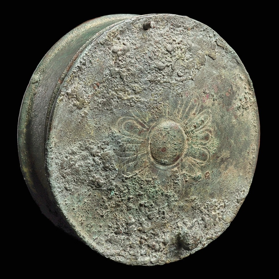 Greek Bronze Lidded Pyxis: Magna Graecia, ca. 5th century BCE. Bronze round lidded container having a large floral element on the center of the lid, and a small ball knob handle. Lid secured with an upright pin hinge. A very ni