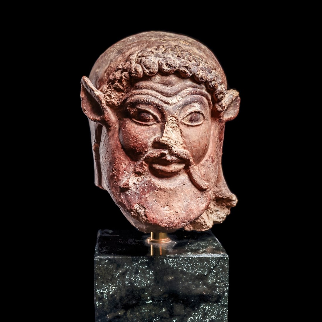 Etruscan Terracotta Satyr Head: Eturia, ca. 500 - 400 BCE. Etruscan molded terracotta satyr's head, possibly from an antefix, a vertical component positioned on the terminal part of a tile above the eaves along the sides of a