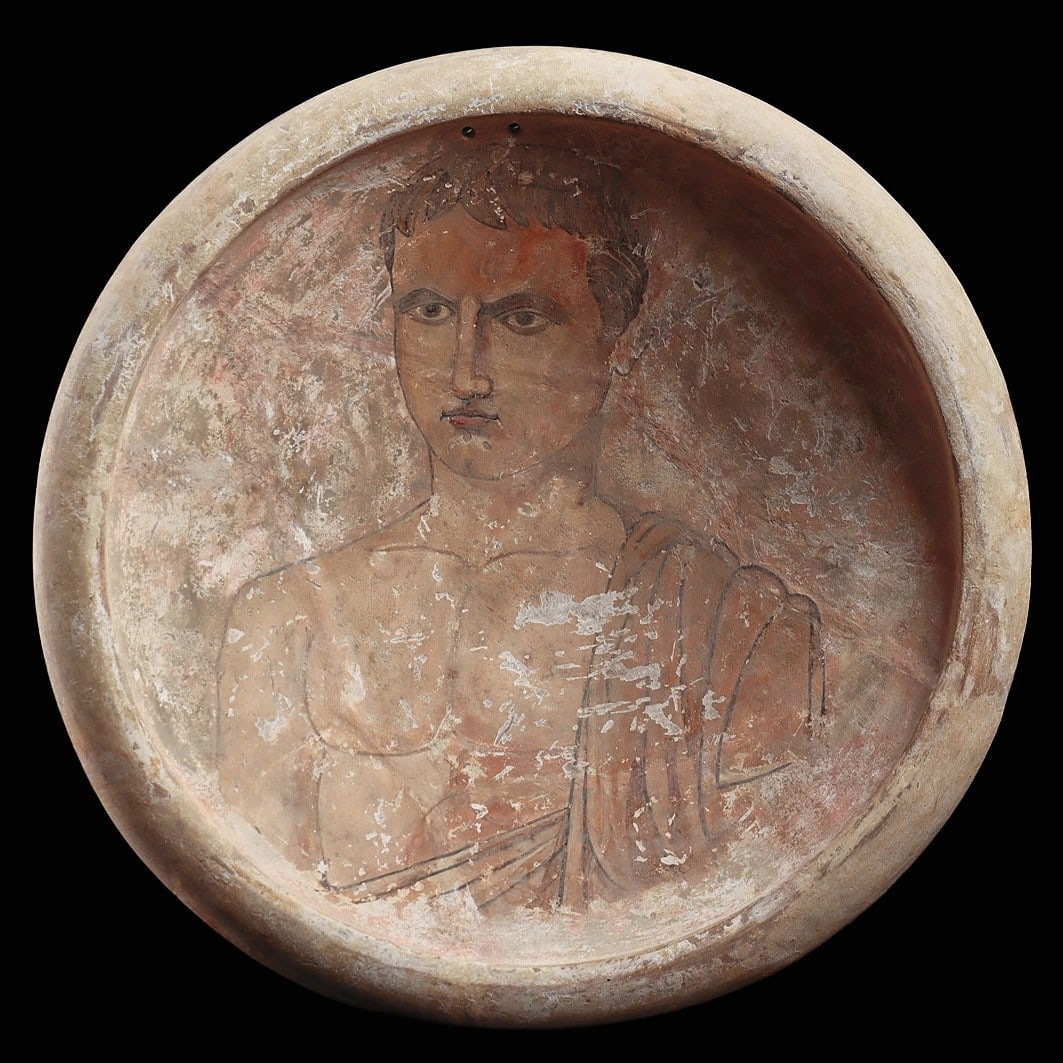 Roman Portrait Plate: Eastern Mediterranean, ca. 1st - 2nd century CE. Pottery deep dish plate having a wide rounded rim. Painted on the interior with a portrait of a male youth, having a curly hairdo and well painted