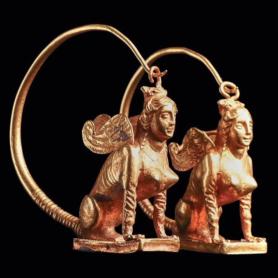 Hellenistic Greco/Roman Gold Winged Sphinx Earrings: Eastern Mediterranean, ca. 150 - 100 BCE. Exceptional matching pair of gold earrings, each in the form of a sphinx with a female head and torso with the body of a lion and wings of an eagle. Each