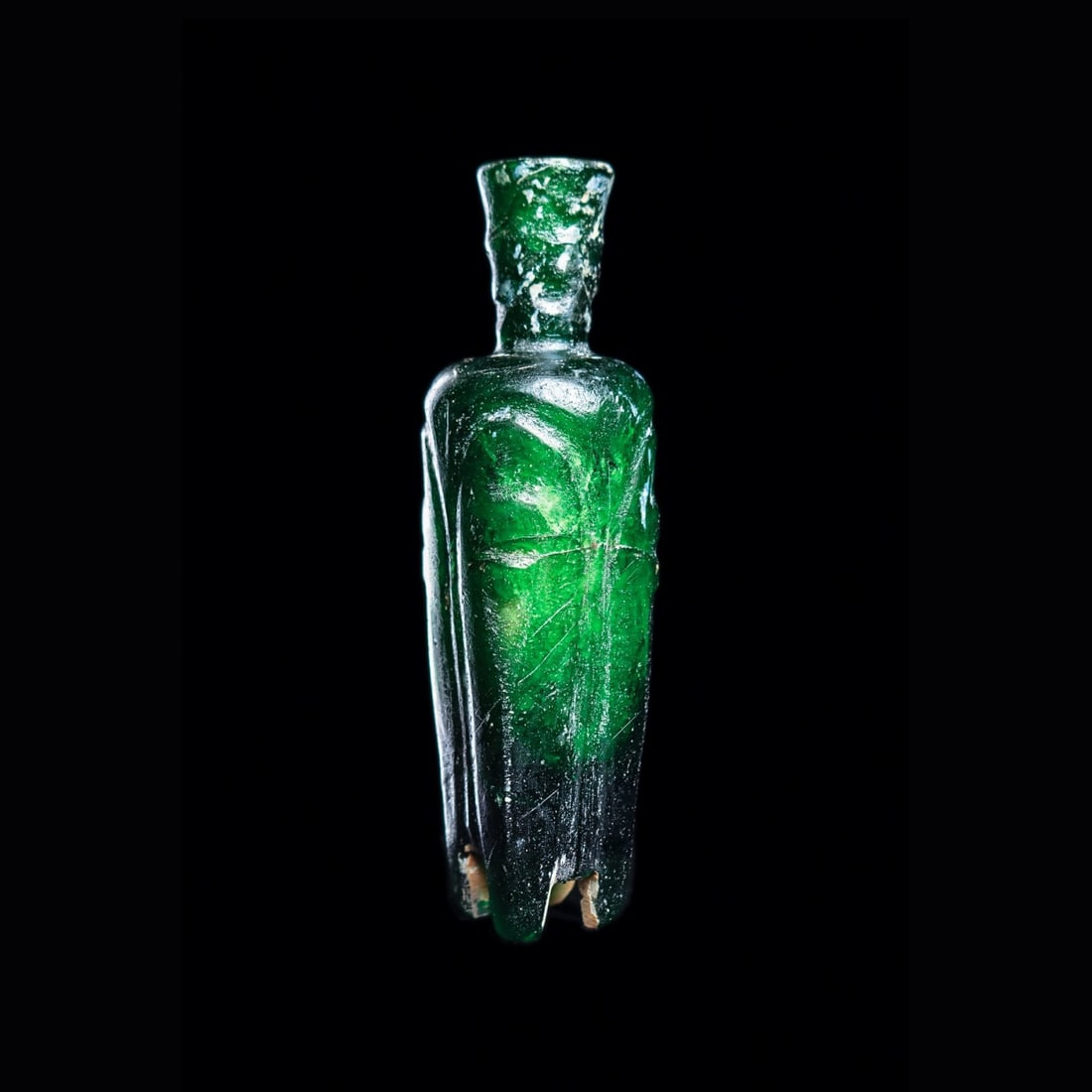 Islamic Molar Glass Vessel: Middle East, ca. 8th - 12th century CE. Rich emerald-green blown glass vial, of tapered rectangular form, with four wheel-cut integral legs. Body is decorated with four cut long tapered vertical panel