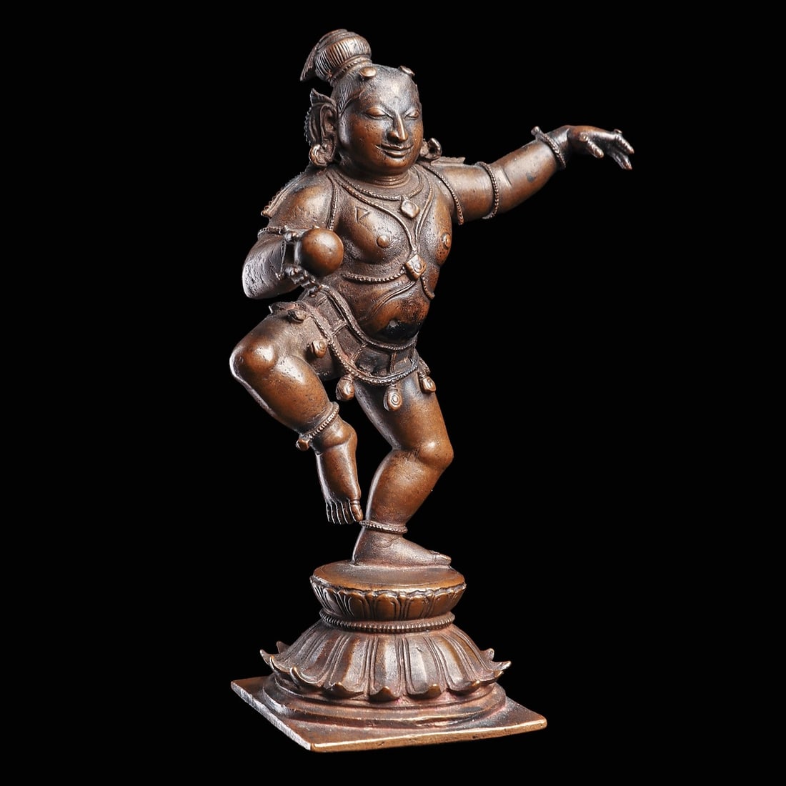 Indian Bronze Dancing Krishna: South India, ca. early 20th century. Solid cast bronze dancing Krishna statue, depicting the deity as a playful child (Bal Krishna) holding a butter ball. Standing on a square pedestal integral lotus 