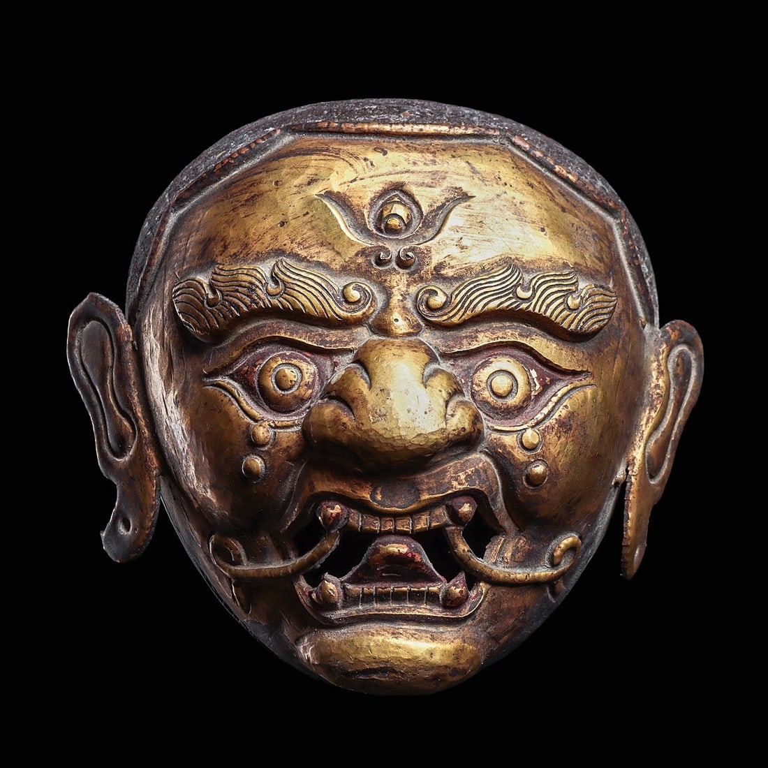Tibetan Large Gilded Copper Head: Tibet, ca. 18th to 19th century. Large gilded copper head having a ferocious expression, highlighted with a black resin painted, incised striated hairdo, flame brows, large eyes, wide wrinkled nose, o