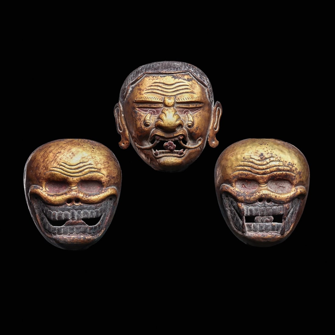 Tibetan Gilded Copper Heads (3): Tibet, ca. 18th - 19th century. Three hollow hammer molded copper votive heads, including a gilded death head with dangling eyeballs, blue-black striated hairdo and having a painful facial expression.