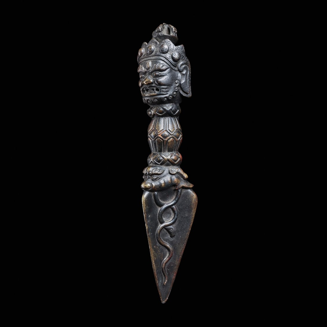 Tibetan Bronze Phurba with Head of Mahacala: Tibet, ca. 19th century. Heavy solid cast bronze phurba, having a highly detailed head of Mahacala wearing a multipointed crown with a dorje finial. Triangular blade with relief intertwined serpents. 