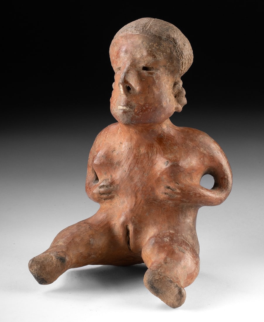 Nayarit Pottery Female Figure - Seated Nude: Pre-Columbian, West Mexico, Nayarit, ca. 300 BCE to 300 CE. A boldly modeled pottery figure depicting a nude female seated with legs splayed and arms bent inward, her hands positioned beneath the brea