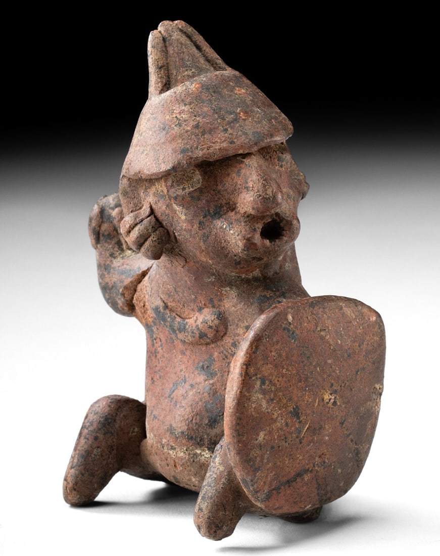 Nayarit Pottery Seated Warrior with Shield: Pre-Columbian, West Mexico, Nayarit culture, ca. 200 BCE to 300 CE. A dynamic Nayarit pottery figure depicting a seated warrior poised for confrontation. The figure sits with knees raised before the b