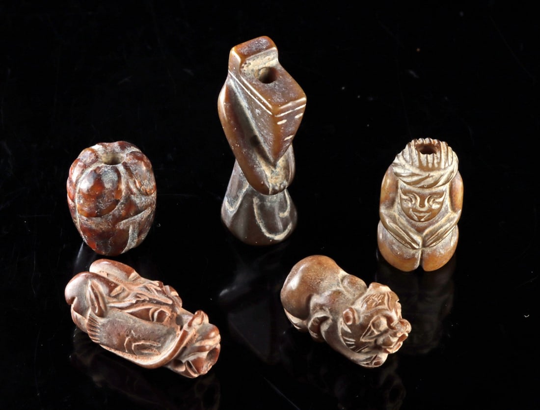 Five Chinese Carved Stone Charm Beads: East Asia, China, ca. 20th century CE. A group of five miniature carved stone bead charms depicting a dragon head, cicada, seated figure, tiger, and an abstract figure, each drilled for suspension. Si