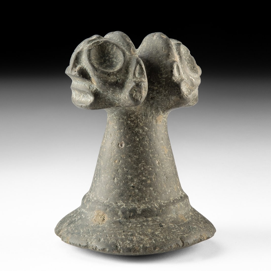 Taino Stone Pestle - Janiform Zemi Heads, Greater Antilles: Pre-Columbian, Greater Antilles, Taino, ca. 1000–1500 CE. A handworked stone pestle whose grip swells into a pair of confronting zemi faces, their bulging concentric eyes and ringed brows carved