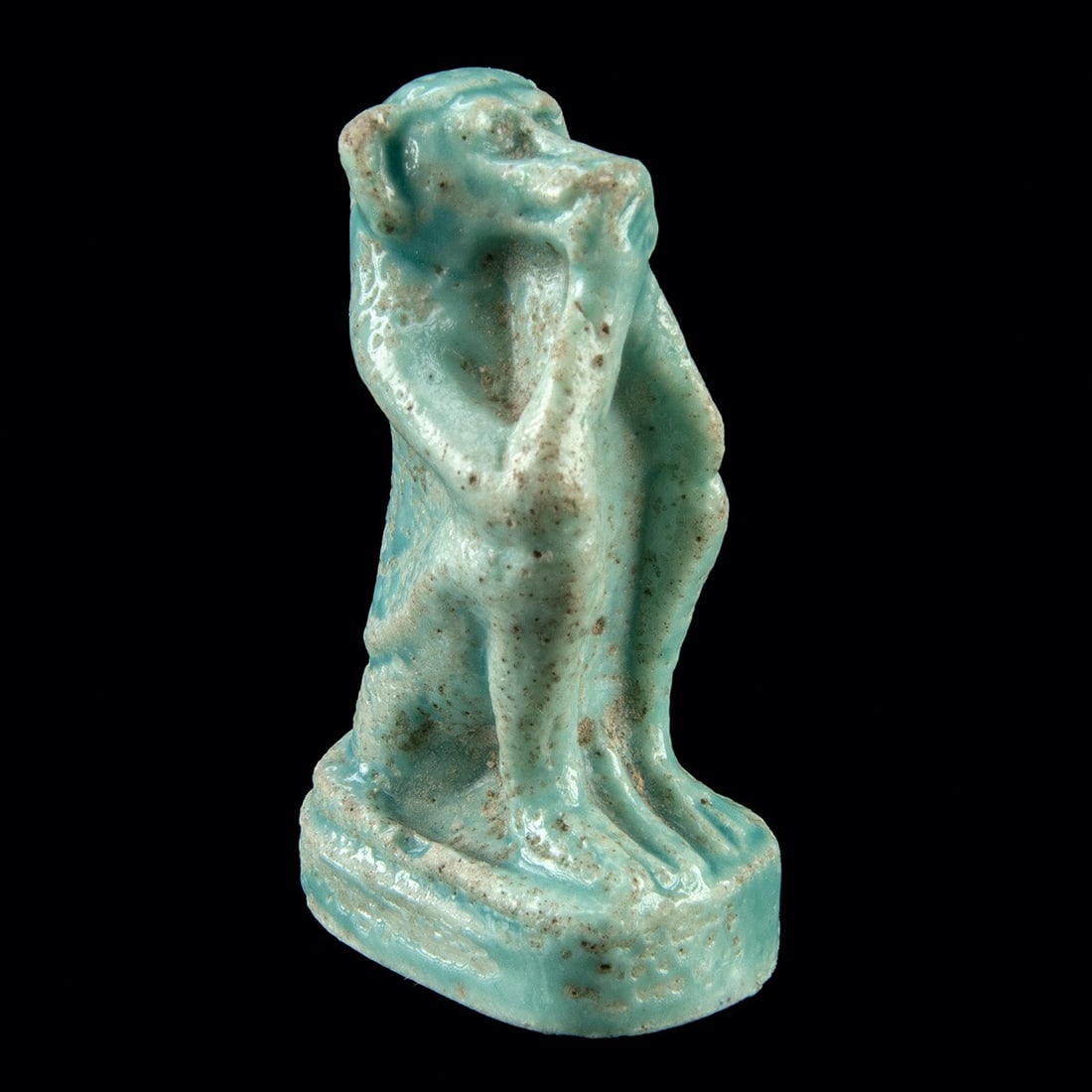 Egyptian Faience Seated Monkey Amulet - TL Tested: Egypt, Middle Kingdom to Late Period, Dynasty XII to XXVI, ca. 1934–614 BCE. A small amulet of pale turquoise faience modeled as a seated monkey, its haunches drawn up and forelimbs reaching tow