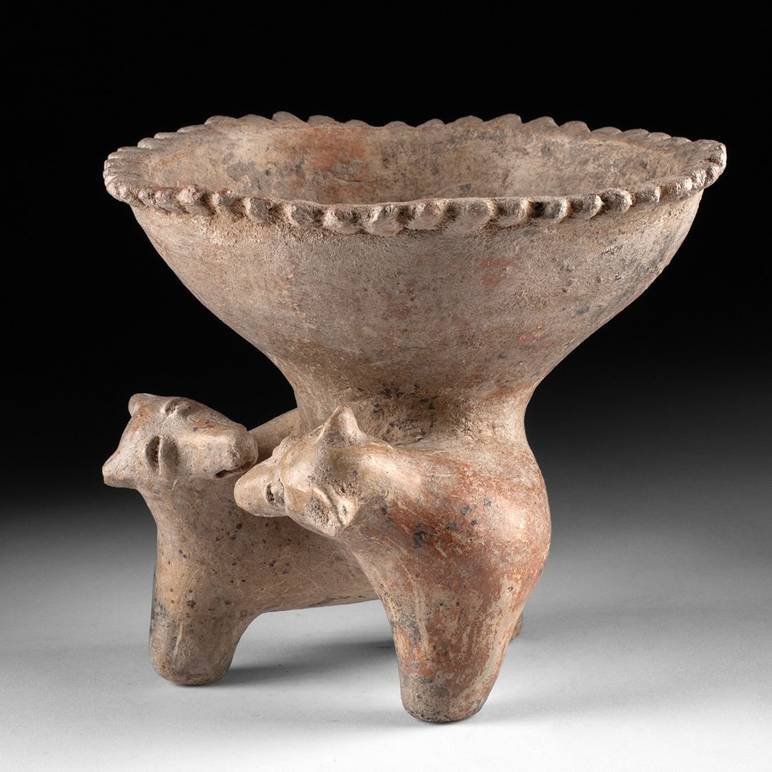 Jalisco Ceramic Tripod Bowl on Double-Headed Dog Base: Pre-Columbian, West Mexico, Jalisco, ca. 300 BCE to 300 CE. A wide-mouthed bowl carried by two canine heads bent toward each other, snouts nearly touching, as though the vessel above them is the subje