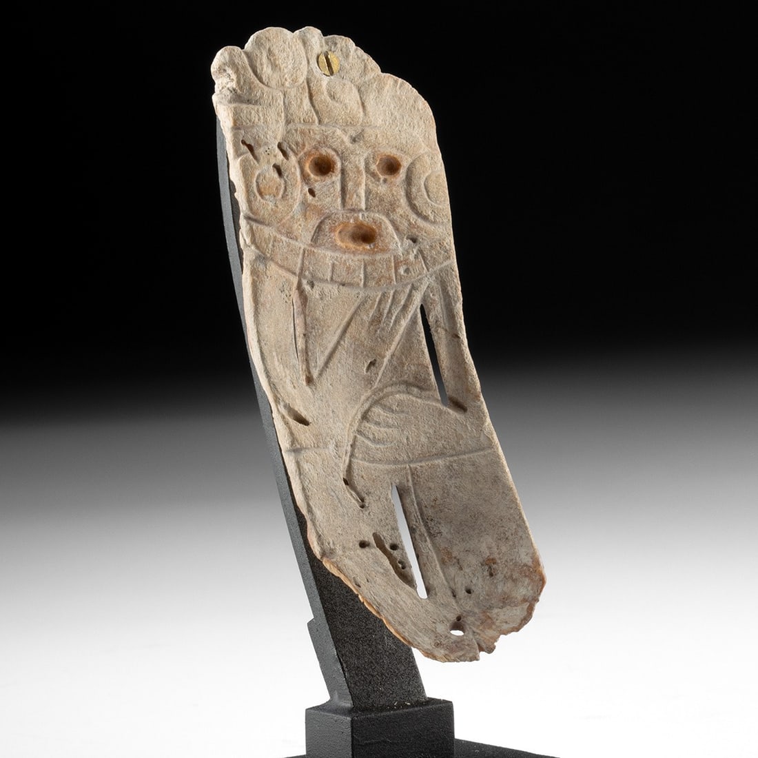 Maya Carved Shell Human Effigy Pendant: Pre-Columbian, Mexico, Maya, ca. 250–900 CE. A carved shell ornament depicting a human figure. The plaque is worked from marine shell, possibly whelk, and shows a frontal face with drilled eyes 