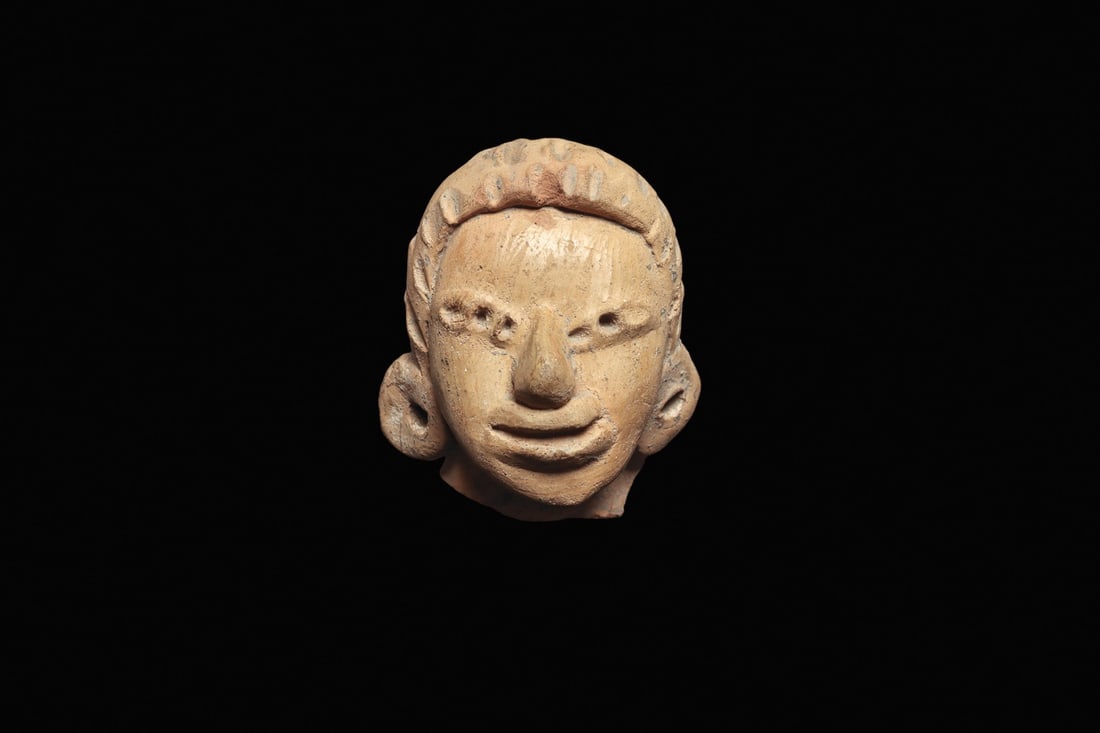Huastec Pottery Figural Head: Panuco River area, Huastec, Mexico, ca. 400–100 BCE. Solid terracotta head from a figure depicted with a stippled textured hairdo, wearing large round ear ornaments. Burnished tan face with seve