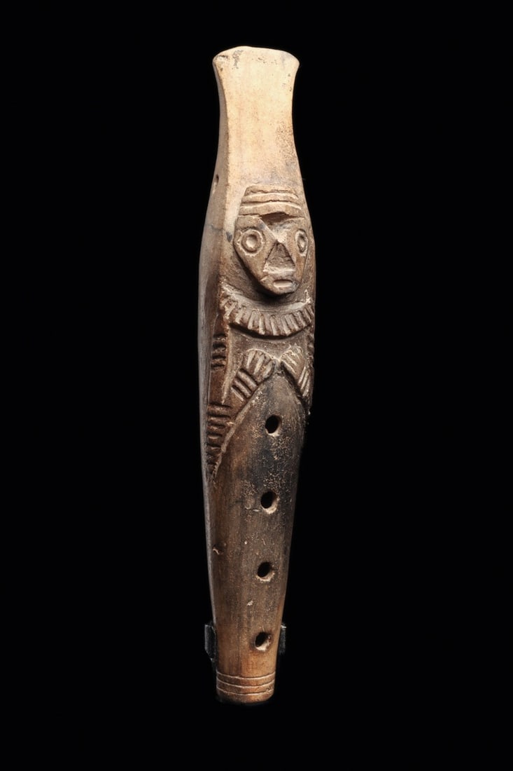 Tairona Pottery Flute with Human Figure: Colombia, ca. 500–1000 CE. Gray-brown color pottery flute depicting a stylized human figure, holding both hands on his chest, having a slightly projecting head with a recessed triangular nose an