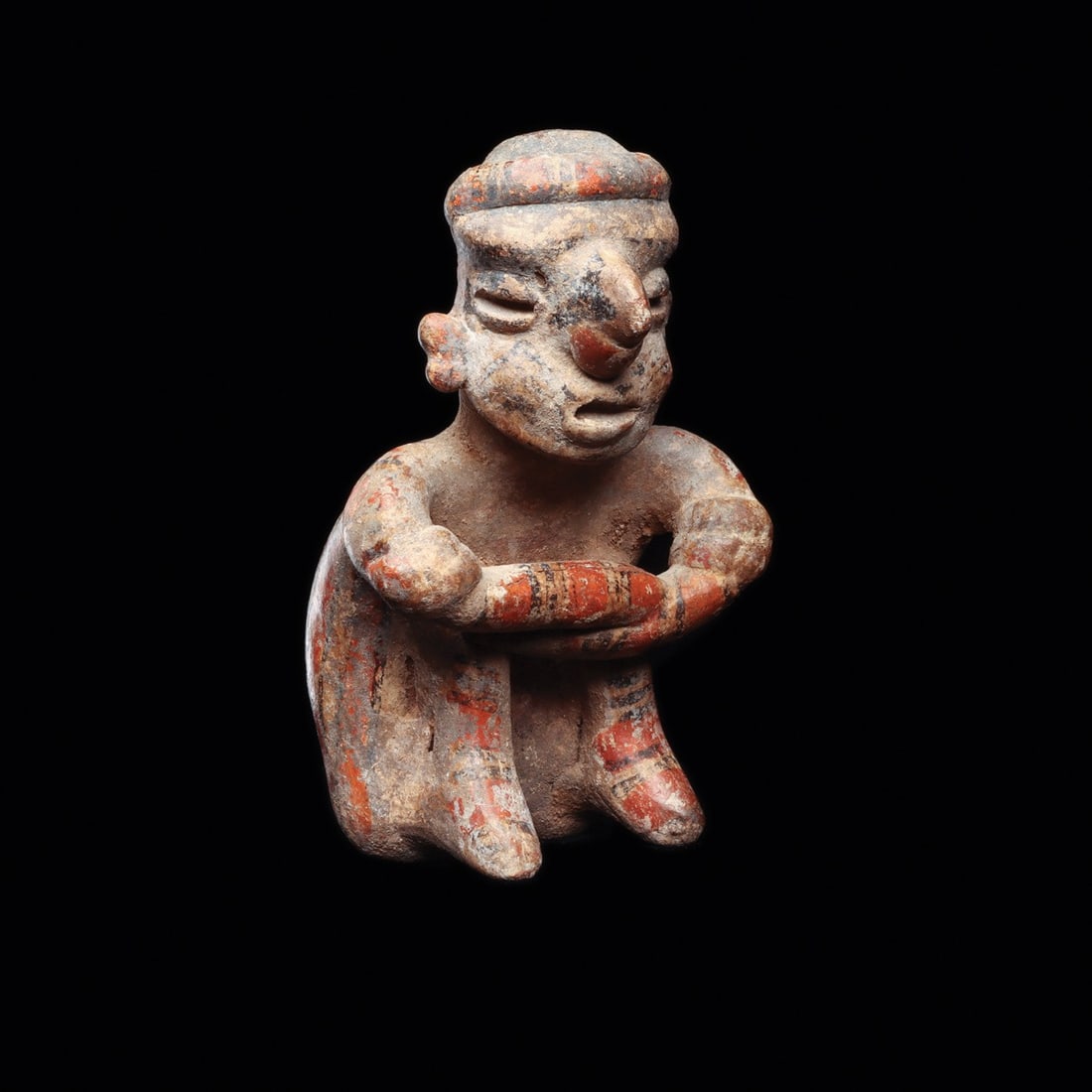Nayarit Seated Figure: Nayarit, ca. 100 BCE – 250 CE. Hollow pottery seated male figure, with knees raised and arms crossed wearing a nose ring and head band. Decorated with red and white stripes, black details to