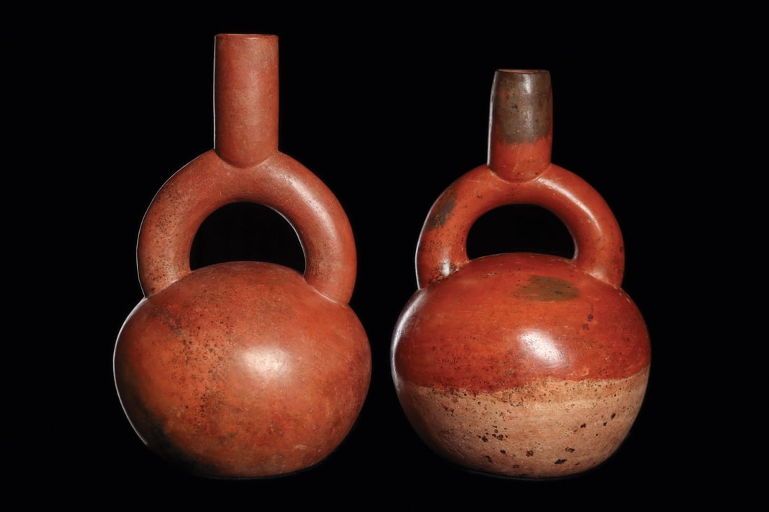 Chavin Stirrup Spout Bottles (2): Chavin, ca. 200 BCE – 200 CE. Two similar pottery bottles, having stirrup type spouts. One decorated with a red-brown painted upper body and a tan-cream lower body. The other bottle is