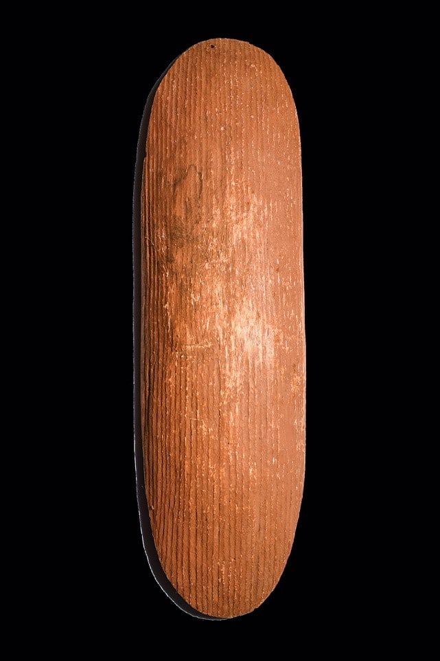 Pitjantjatjara or Aranda Beanwood Parrying Shield: Central Australia. Possibly stone cut, carved of soft beanwood with convex obverse, fluted lengthwise on both sides, thinly tapered at edges, hollowed grip in center, and both sides covered with red