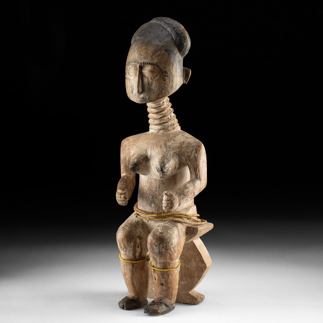 African Fante Wood Figure - Seated Queen Mother with Bead Strands: West Africa, Ghana, Fante, ca. 1900–1930 CE. A seated female figure carved from a single block of wood, representing a Fante queen mother. The surface is coated in white kaolin, with black pigme