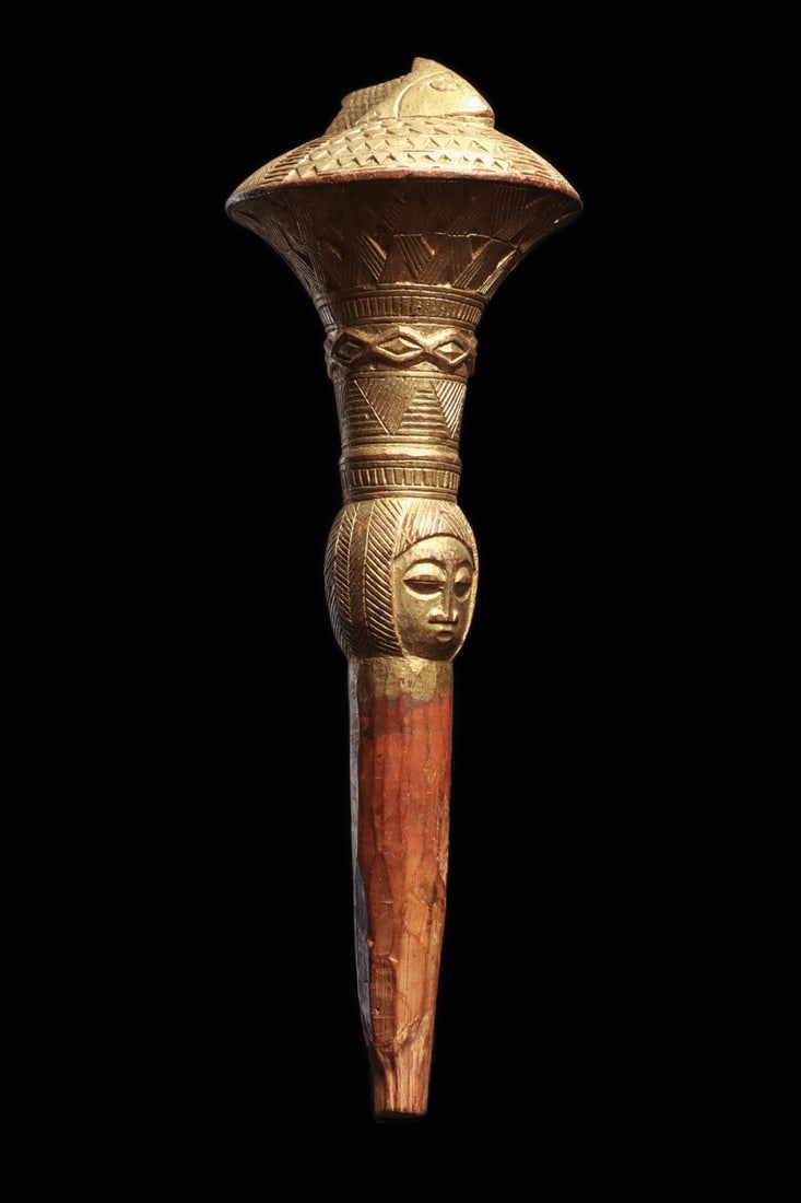Akan Gilt Staff Finial: Ghana. Carved wood staff finial presenting a fish at top, possibly a mudfish, and two opposing human faces above the grip. Fine linear engraved pattern along support. The finial is a badge of office