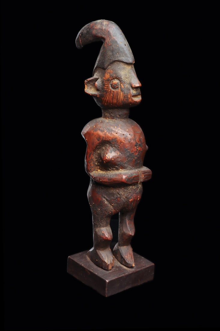 Eshu Figure: Nigeria. Yoruba figure carved for the devotion of Eshu, the female stands wearing the headdress, having large hollowed ears, long scarification lines cover the sides of the face, torso of thick propor