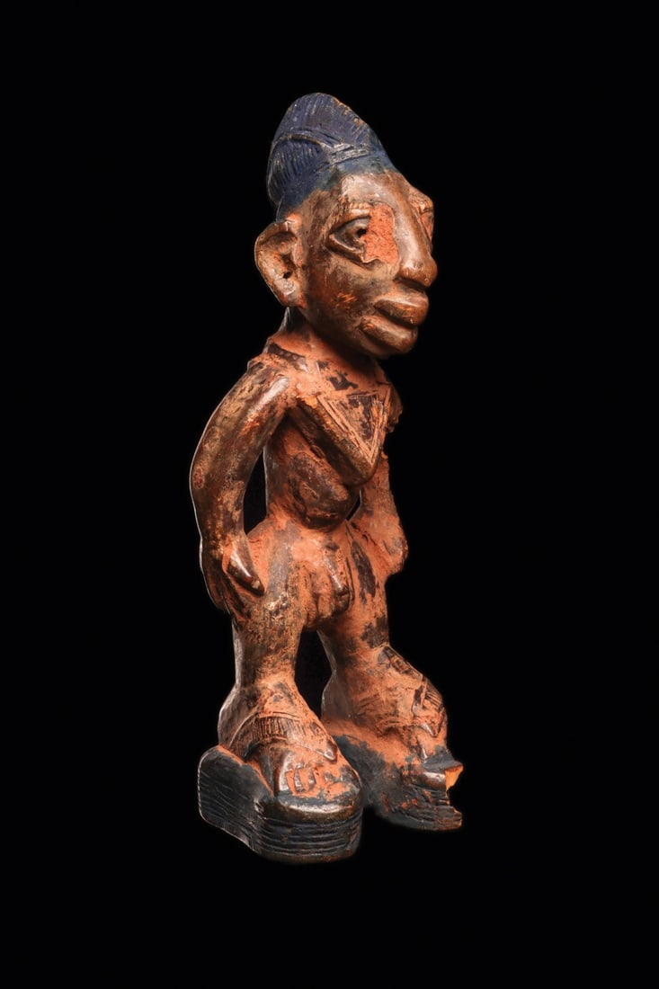 Yoruba Ibeji Twin Figure: Nigeria, early to mid 20th century. Male twin statuette (Ere Ibeji), from the Igbomina region, standing in a wide stance with individual enlarged feet supported by platform shoes, and a necklace with